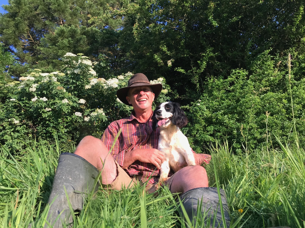 Andy Fields sitting in long grass with his dog at Bradford Farm surrounded by trees and wildlife