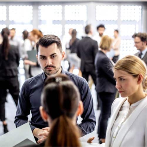 Business professionals engaging in conversation at a busy trade show stand with multiple interactions taking place