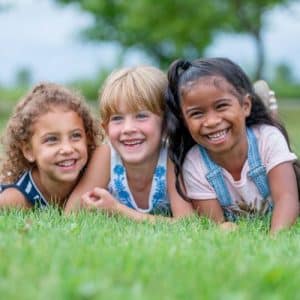 Three smiling children lying on grass outdoors during an environmental education activity focused on nature and sustainability